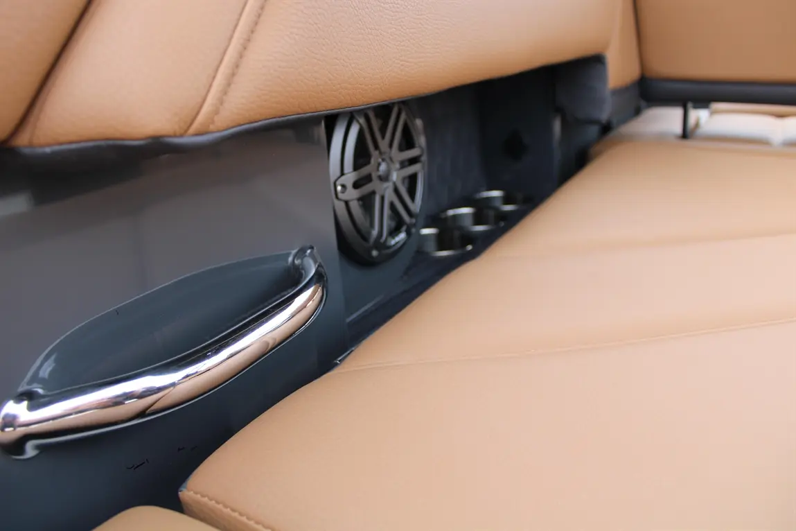 Close-up of a luxury car seat with tan leather, featuring a chrome handle, speaker, and drink holders.